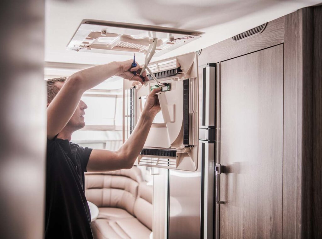 White man with blonde hair fixing caravan air conditioning electrics inside the caravan