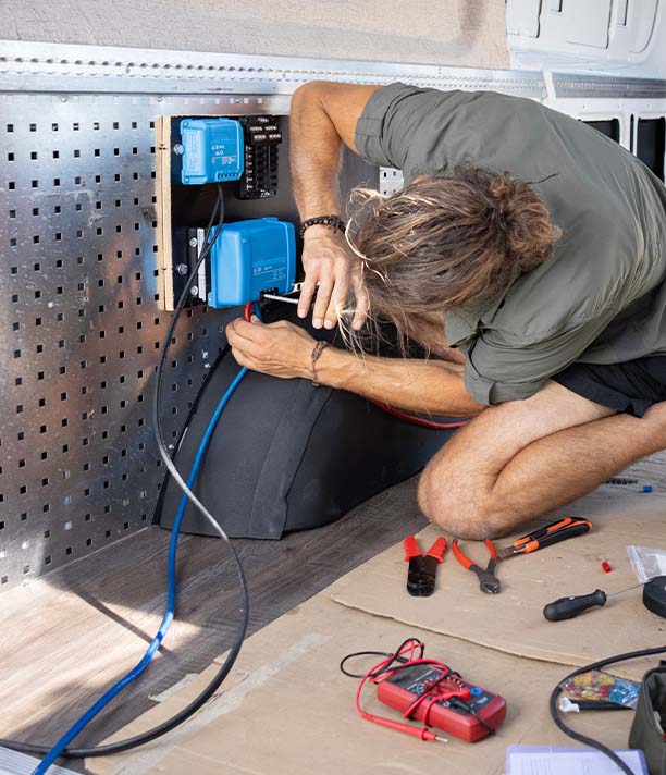 White man with blonde hair installing a blue battery electrics system in the back of a caravan.